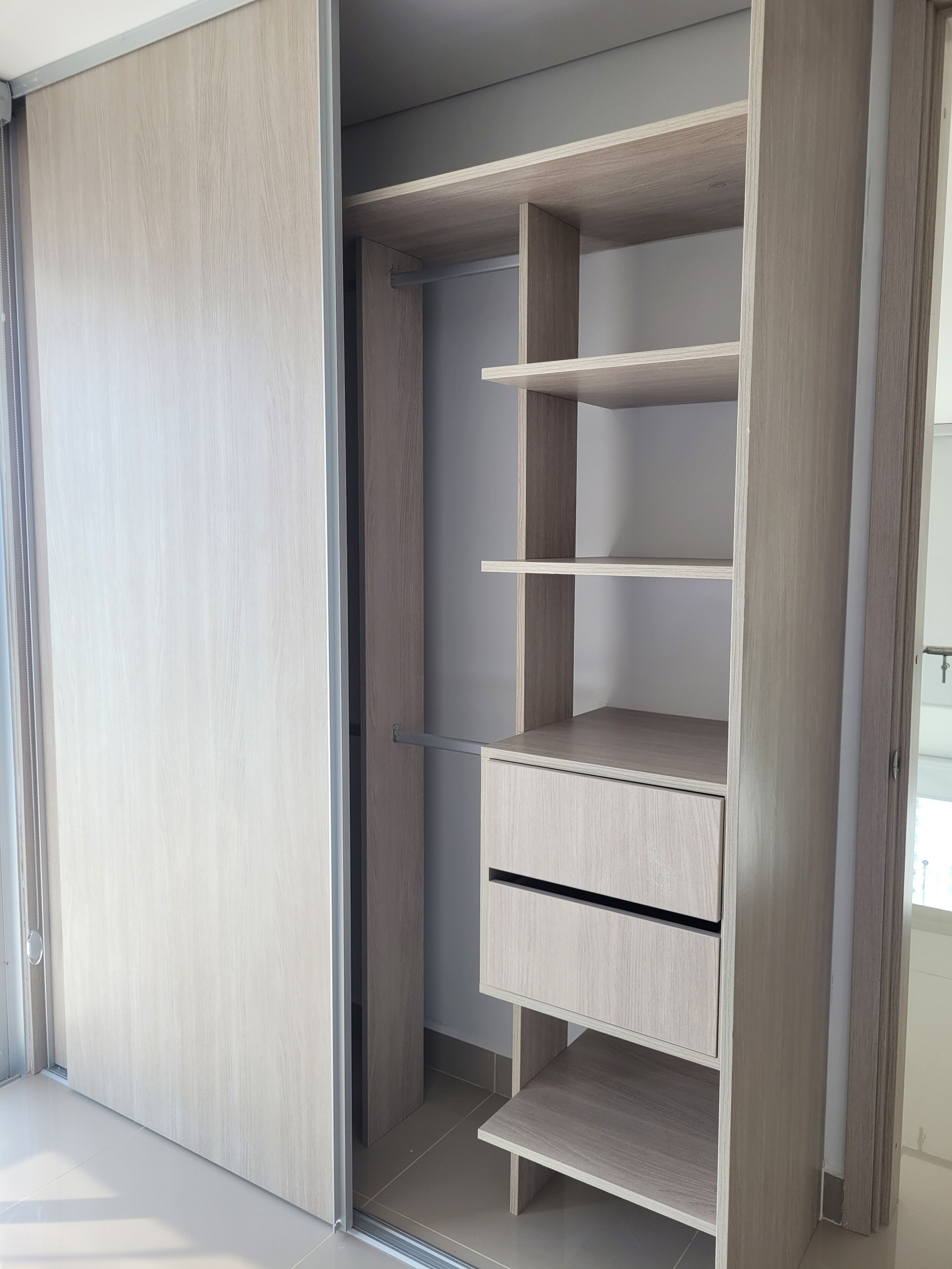 A modern closet with multiple shelves and drawers, featuring a light wood finish and a sliding door.