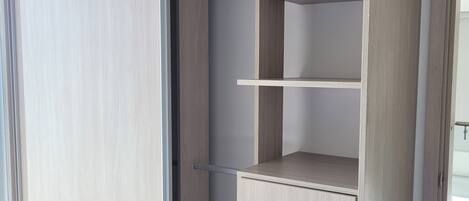 A modern closet with multiple shelves and drawers, featuring a light wood finish and a sliding door.