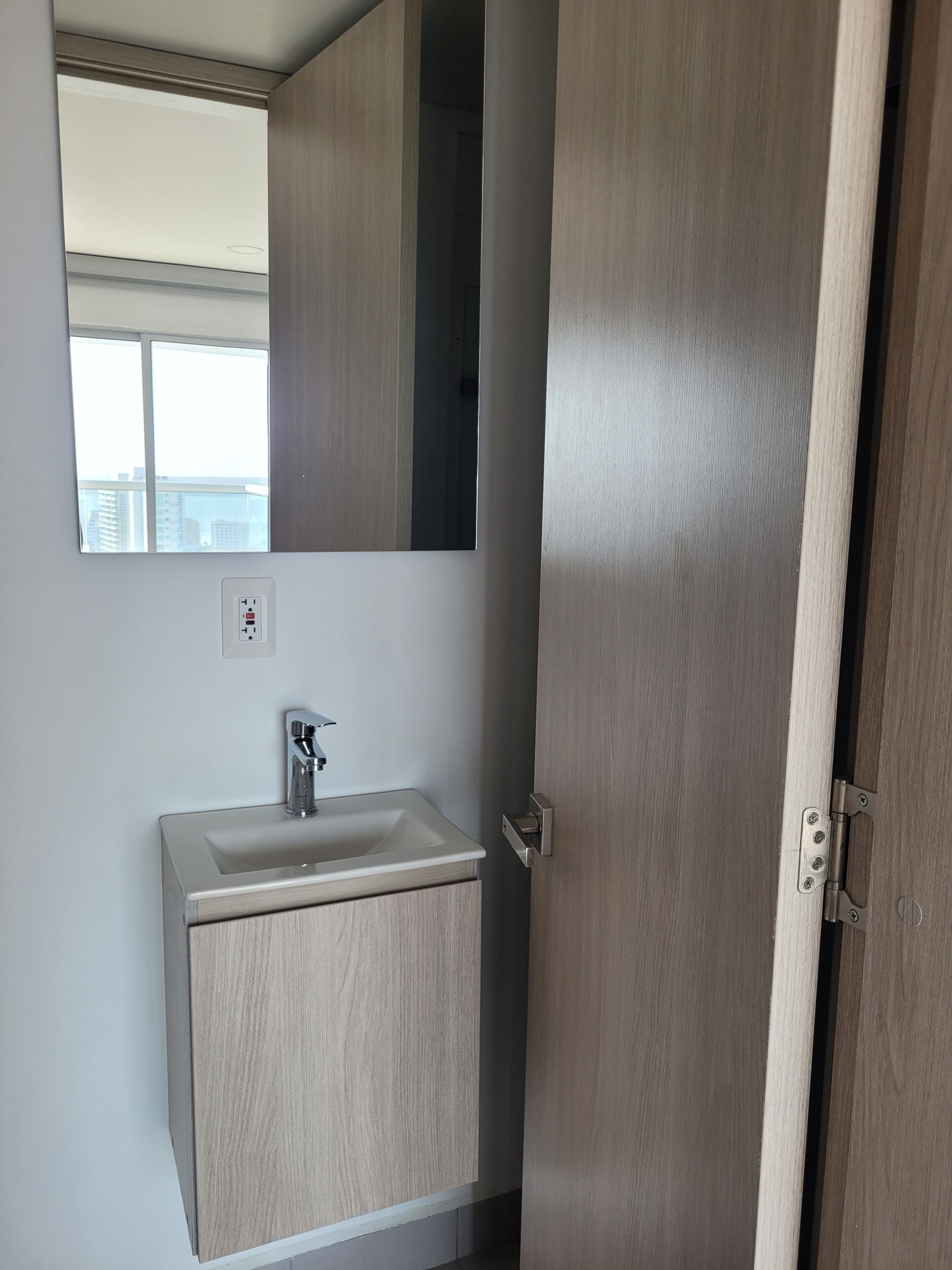 Un baño con lavamanos, espejo y puerta de madera.