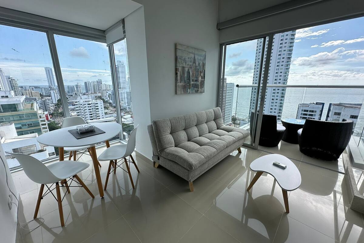 A modern living room with a sofa, a dining table with chairs, and a view of the city and water.