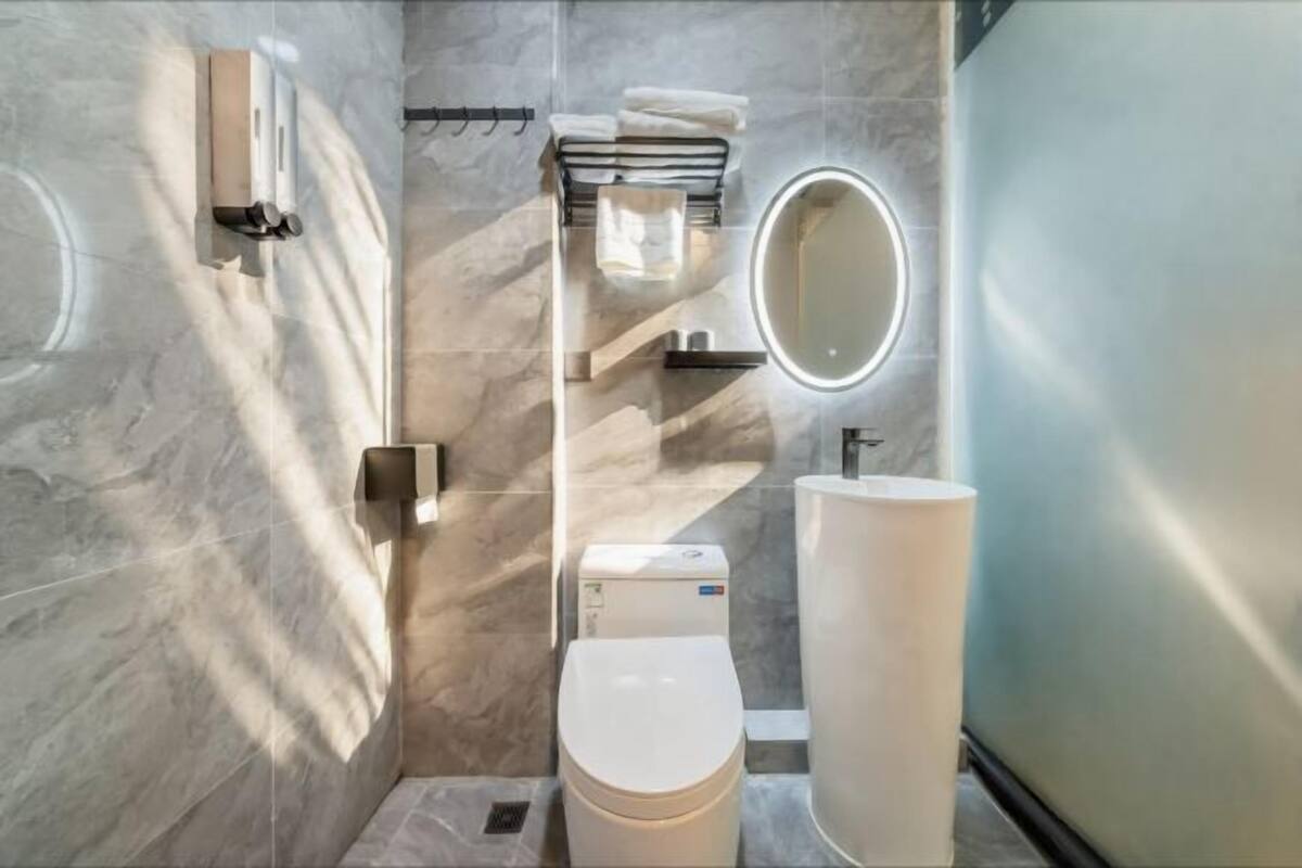 Un baño moderno con inodoro, lavamanos, perchero para toallas y espejo.