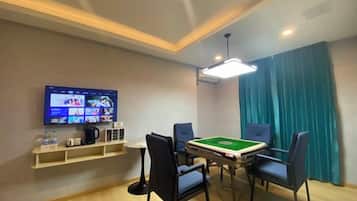 A room with a pool table, chairs, a television mounted on the wall, and a shelf with items.