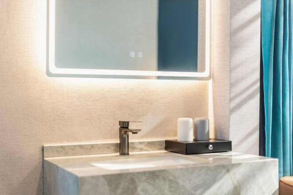 Un baño moderno con lavamanos de mármol, un grifo, un espejo con iluminación integrada y un dispensador de jabón negro.