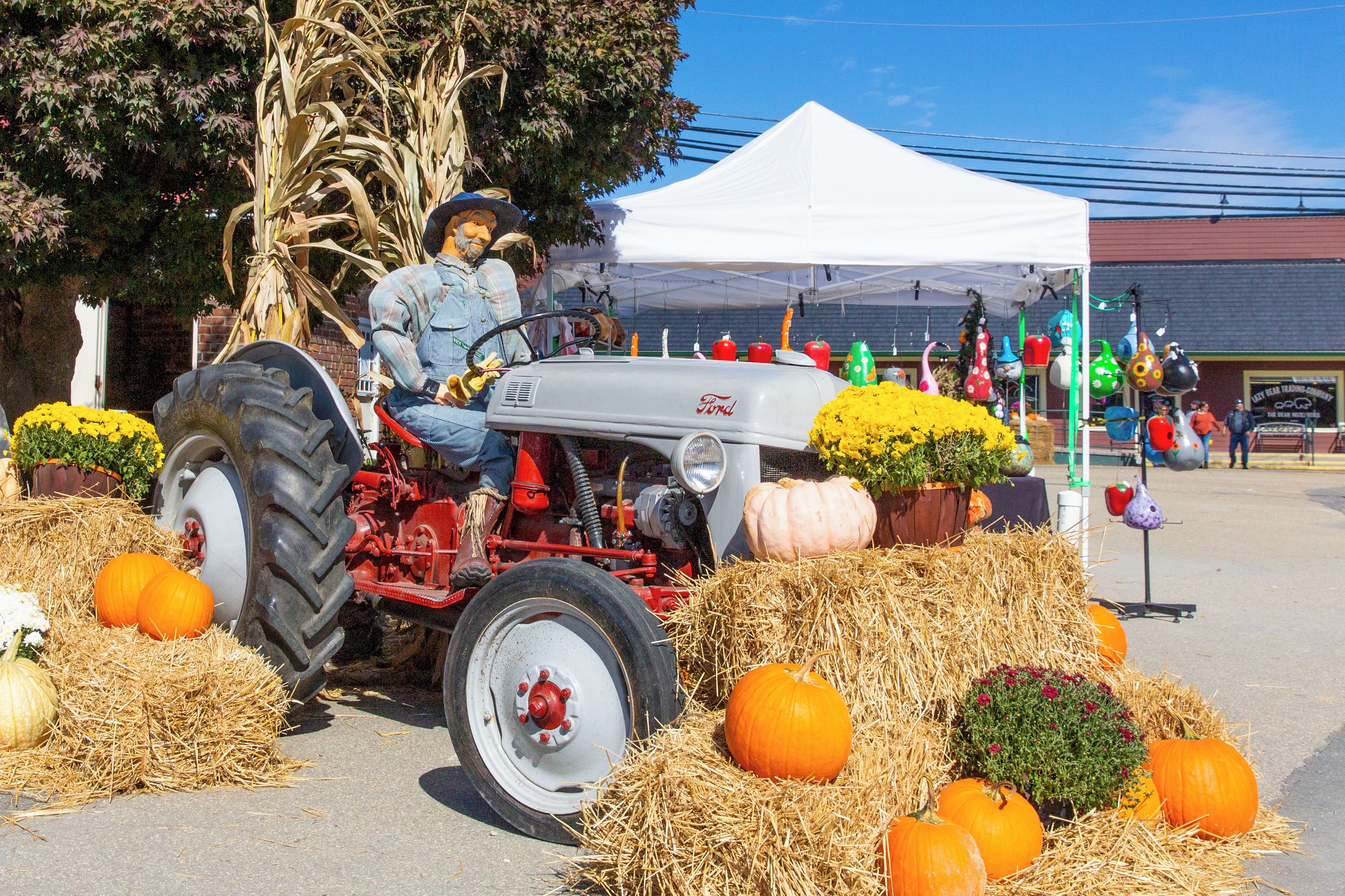 A vintage tractor with hay bales and pumpkins in a display area.
