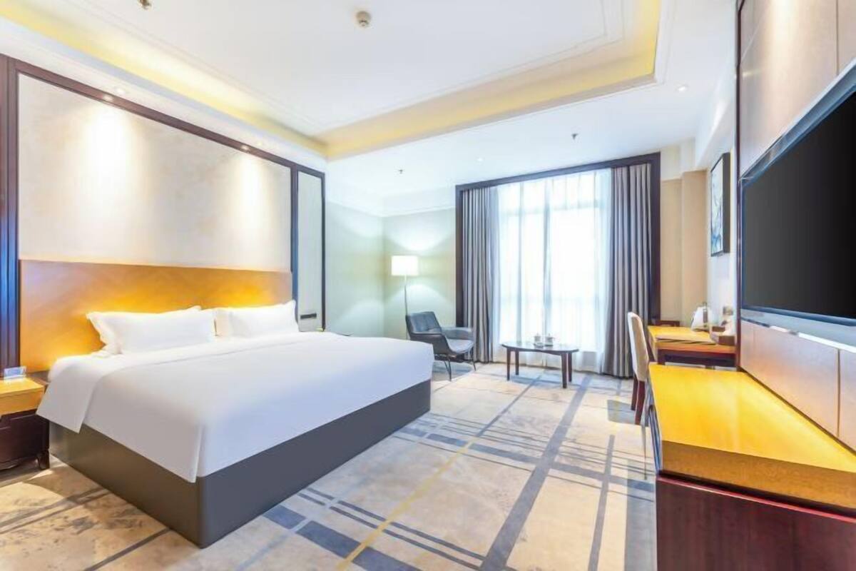 A hotel room with a large bed, a desk with a chair, a television, and a window with curtains.