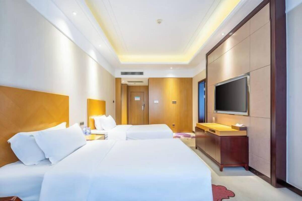 A hotel room with two beds, a TV, a desk with a chair, and a wooden wardrobe.
