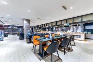 Un restaurante moderno con varias mesas y sillas, una zona de cocina y un área de estar con vistas a la ciudad.
