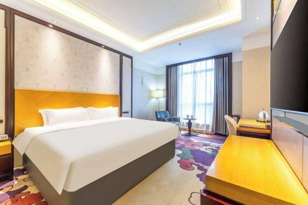 A hotel room with a large bed, a desk, a chair, a TV, and a window with curtains.