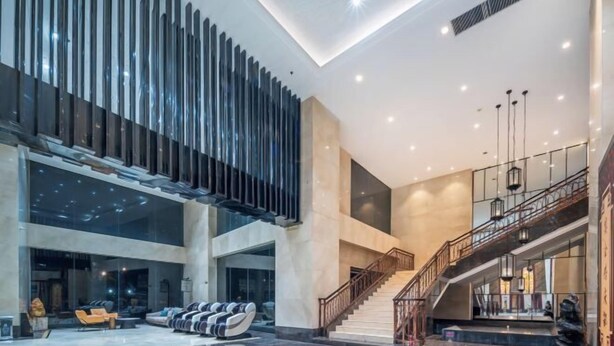 A spacious lobby with a modern design, featuring a seating area, a staircase, and a large glass wall. - Shuiyi Jianianhua Hotel (Juancheng)