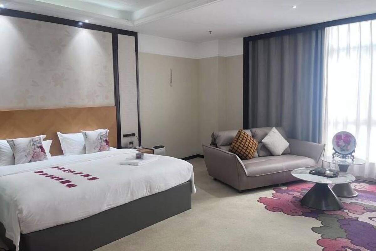 A hotel room with a bed, a sofa, a coffee table, and a large window with curtains.