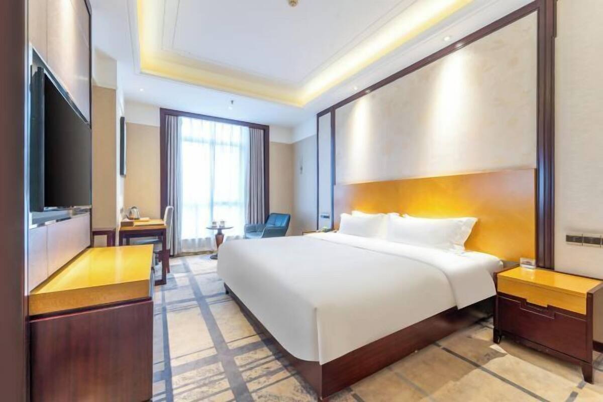 A hotel room with a large bed, a desk, a chair, a TV, and a window with curtains.