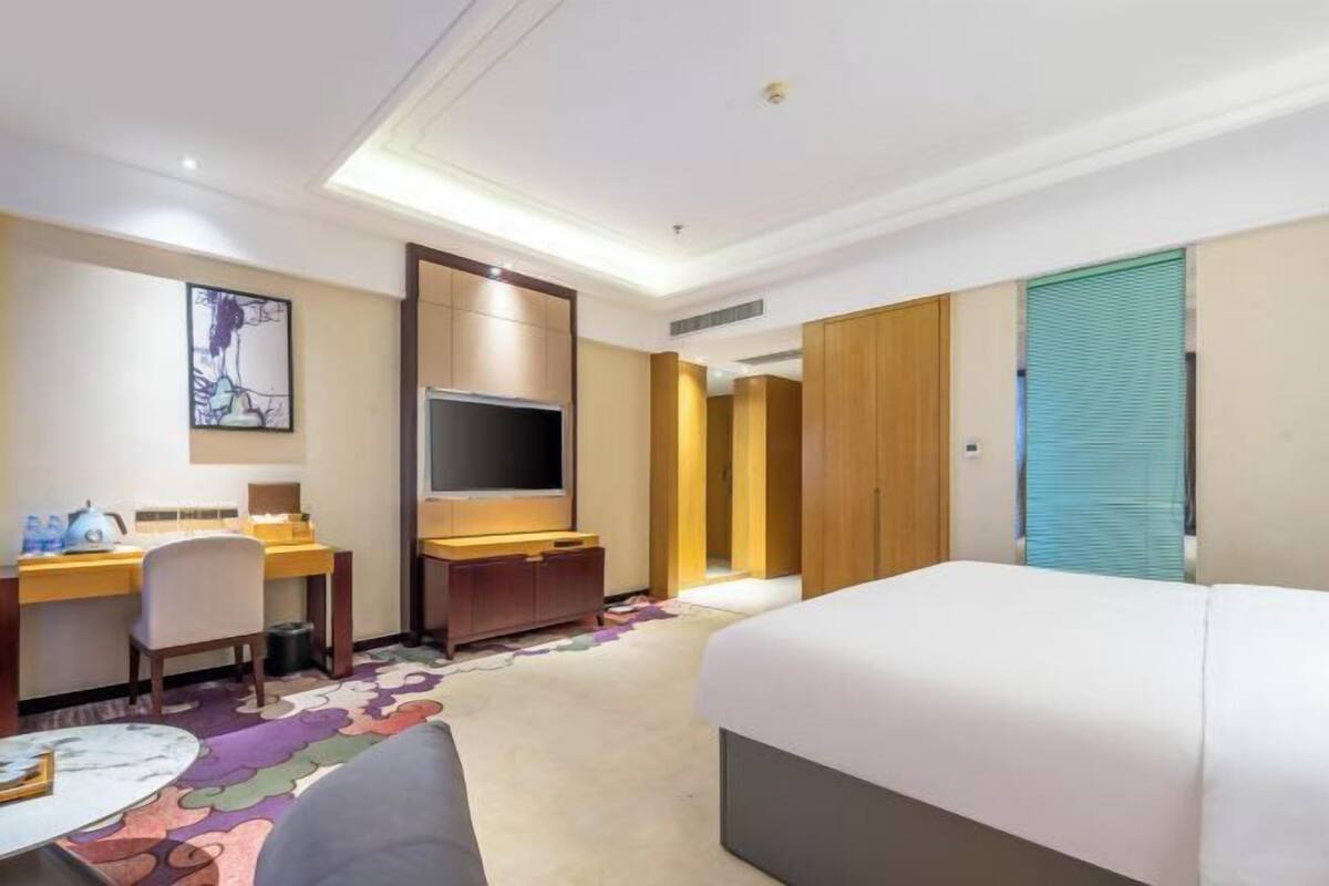 A hotel room with a bed, desk, chair, television, and a colorful carpet.