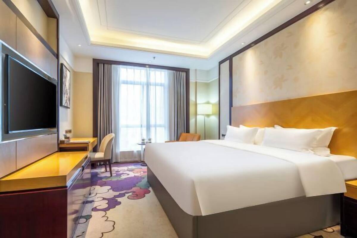 A hotel room with a bed, a TV, a desk, and a chair.