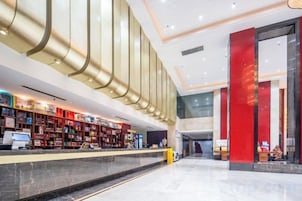 Un vestíbulo de hotel con una recepción, un pilar rojo grande y una decoración de diseño moderno.