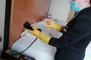 A person in a black jacket and yellow gloves using a device on a bed.