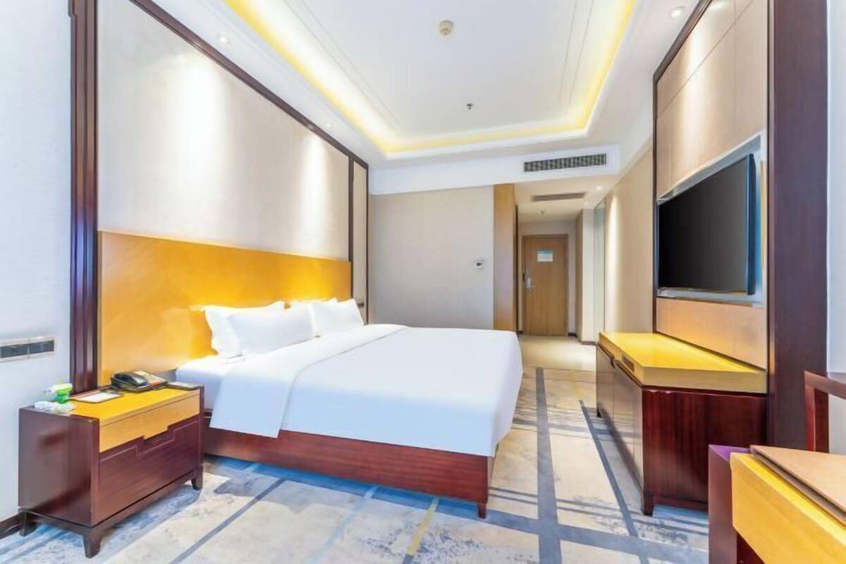 A hotel room with a bed, bedside table, TV, and a carpeted floor.