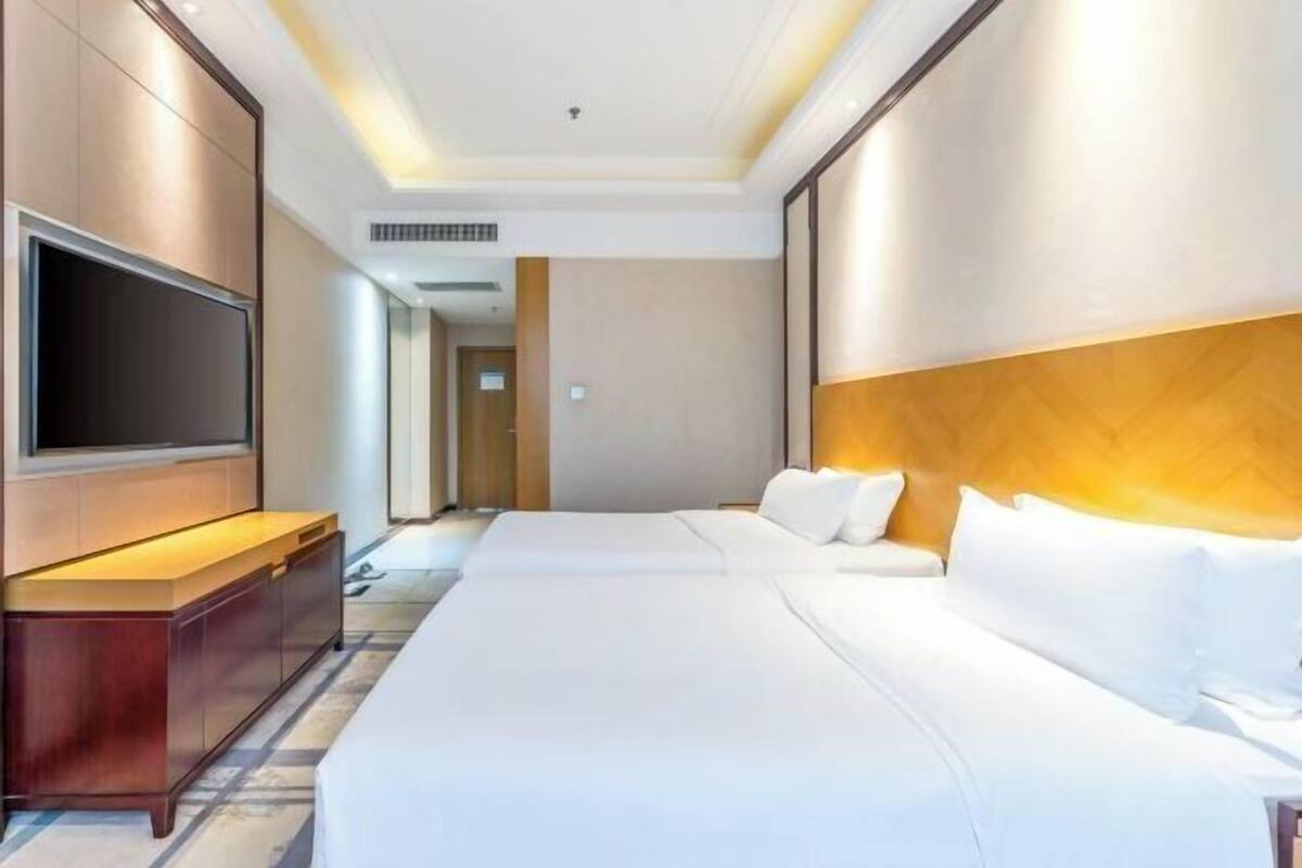 A hotel room with a large bed, a TV, a wooden headboard, and a built-in TV cabinet.