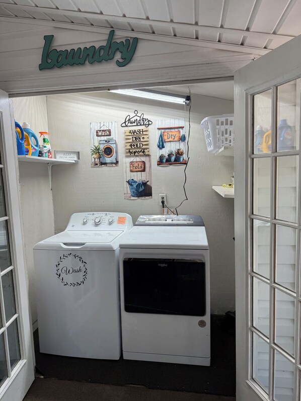 A laundry room with two front-loading washers, a wall-mounted drying rack, and various laundry supplies. - Charming 2-bedroom house in Monroeville with Wi-Fi and AC. (Monroeville)