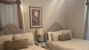 Un dormitorio con dos camas, un ventilador de techo, un cuadro enmarcado y una mesita de noche con una lámpara.