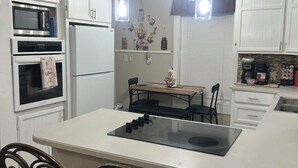 Una cocina moderna con armarios blancos, una isla central con placa de inducción negra y una zona de comedor con mesa y cuatro sillas.