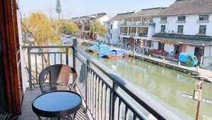 A balcony with wicker chairs and a table overlooking a canal with boats and traditional buildings. - Zhouzhuang Jingou Linhe Bieyuan Chinese Inn (Kunshan)