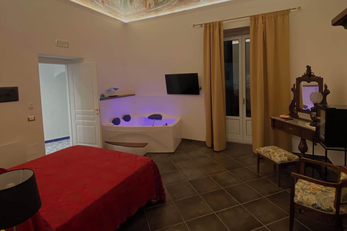 A room with a red bed, a bathtub, a desk, and a chair.