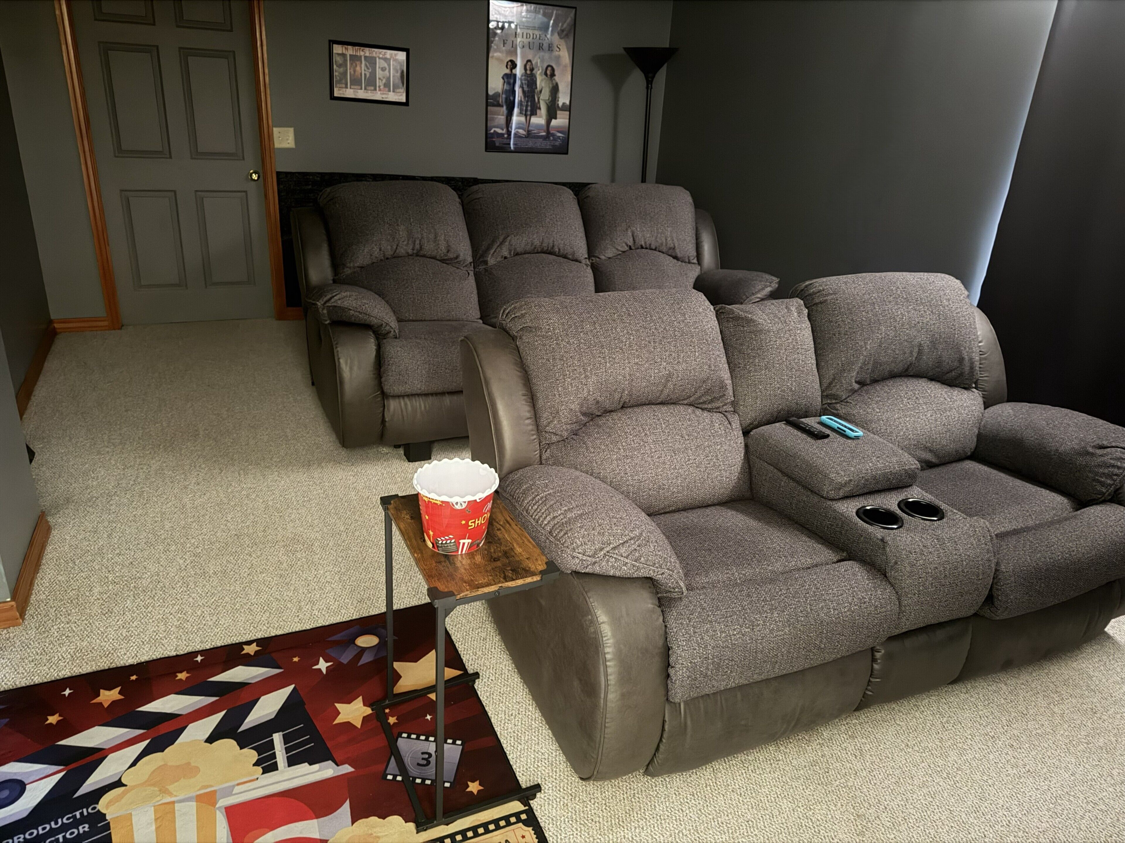 A home theater room with two recliner sofas, a popcorn bucket, and a movie poster on the floor.