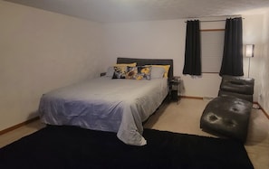 Une chambre à coucher avec un lit, une chaise, une table de chevet et une fenêtre avec des rideaux.