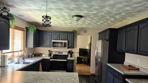 A modern kitchen with dark cabinets, a central island, stainless steel appliances, and a textured ceiling.