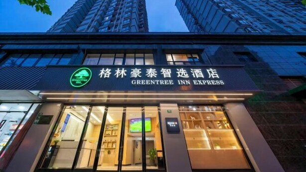 The exterior of the GreenTree Inn Express hotel with a sign in both English and Chinese, large windows, and a view of the surrounding high-rise buildings. - GreenTree Inn Express (Shanghai City God's Temple BundYu Garden subway station shop) (Shanghai)