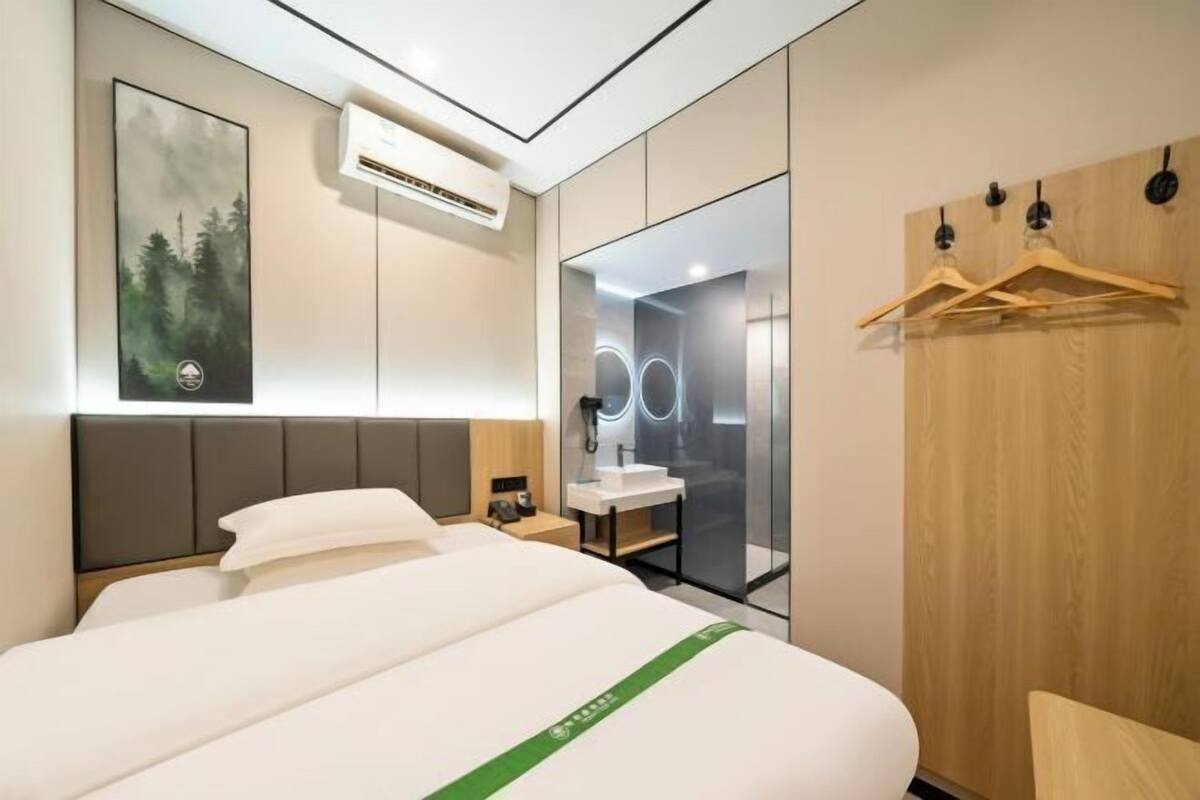 A modern hotel room with a bed, a mirror, a vanity, and a coat rack.