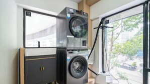 A compact laundry room with a front-loading washing machine, a dryer, and a window with a view of the street. - GreenTree Inn Express (Shanghai City God's Temple BundYu Garden subway station shop) (Shanghai)
