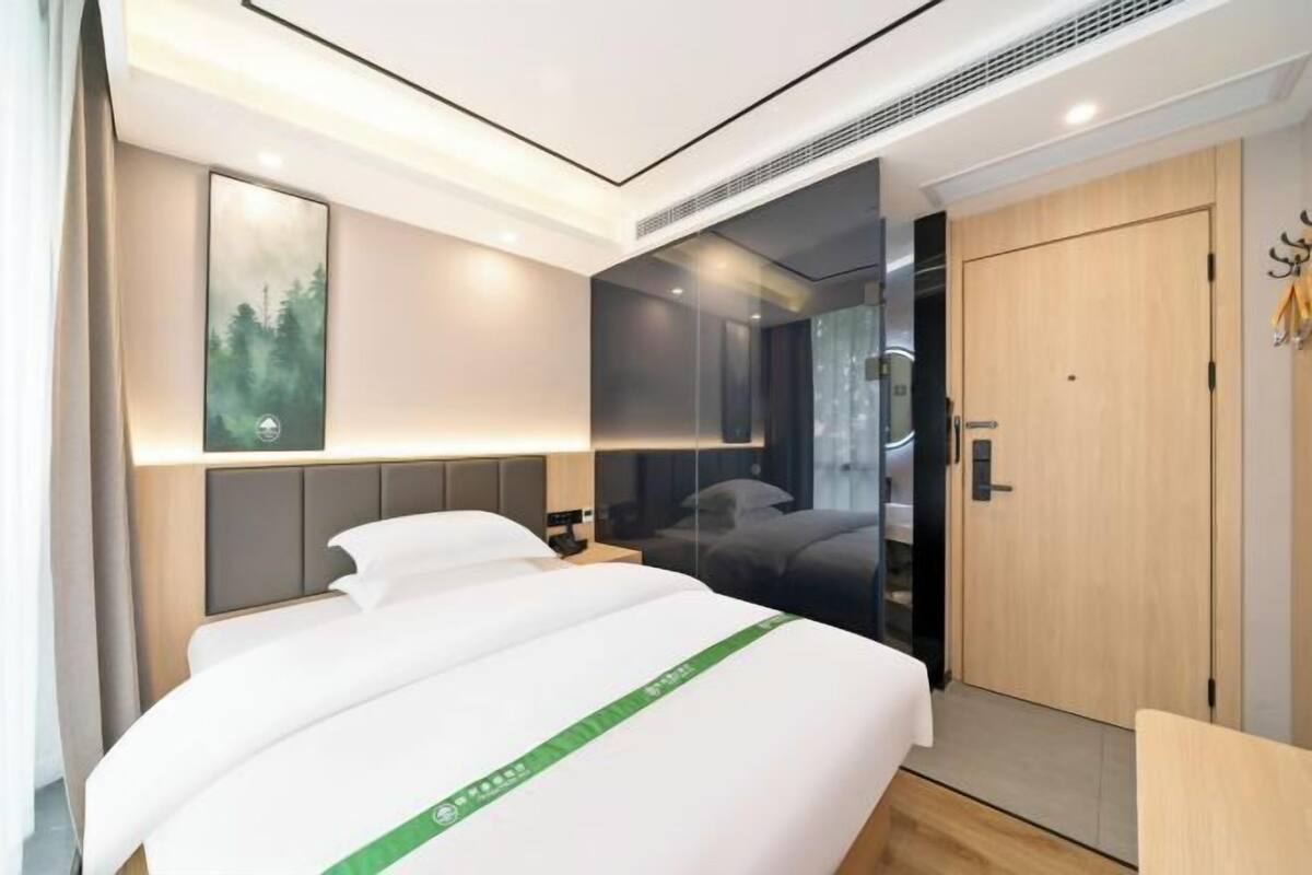 A modern hotel room with a large bed, a mirror, a wooden door, and a view of the outdoors.