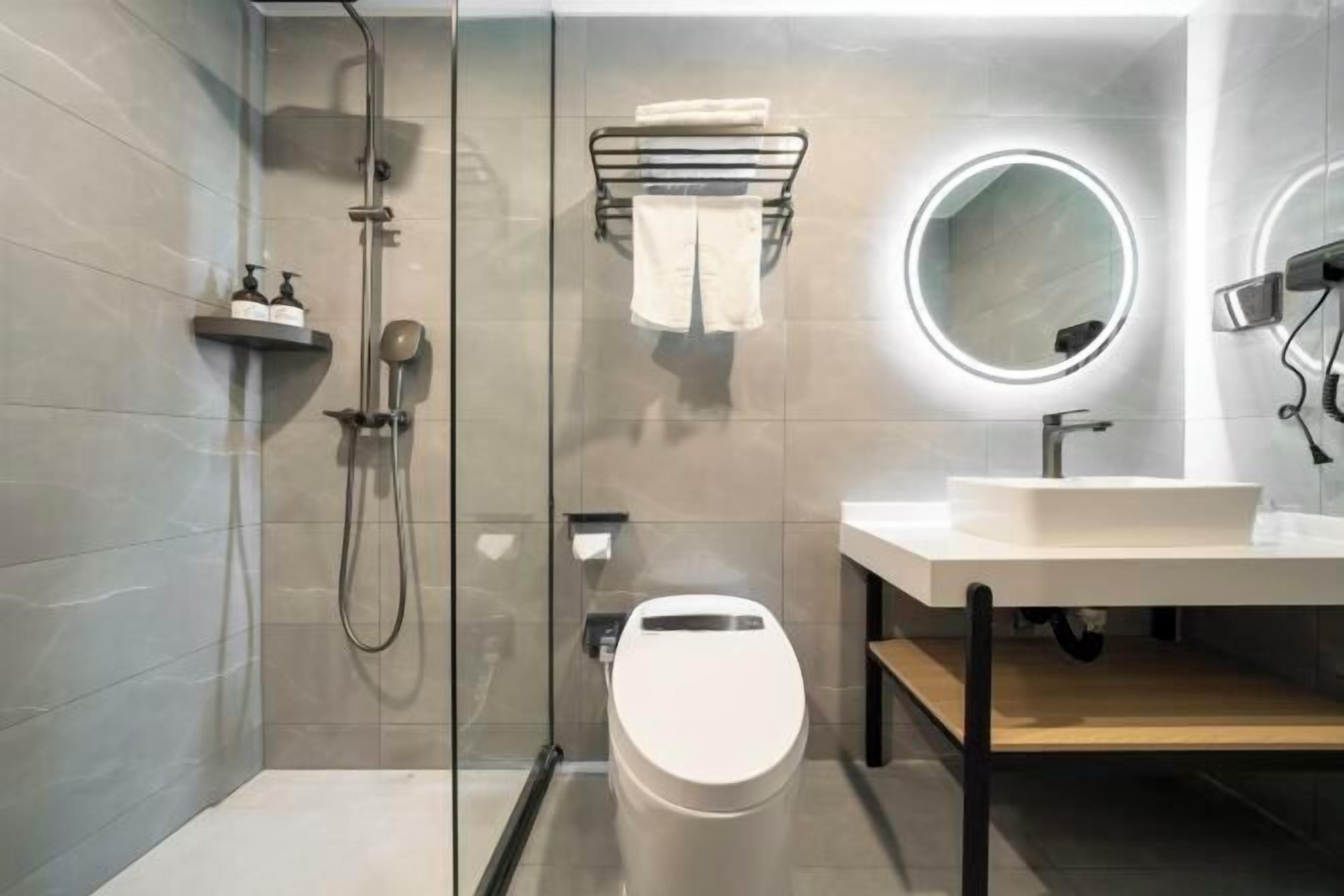 Un baño moderno con ducha envuelta en vidrio, inodoro blanco, lavamanos con espejo y un perchero para toallas.
