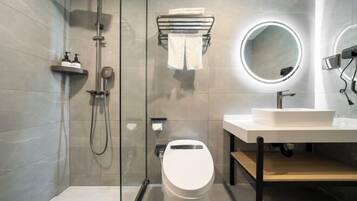 Un baño moderno con ducha envuelta en vidrio, inodoro blanco, lavamanos con espejo y un perchero para toallas.