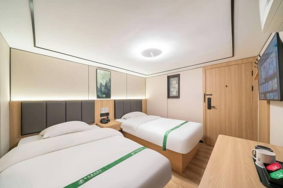 A hotel room with two beds, a wooden desk, a television, and a nightstand with a lamp.