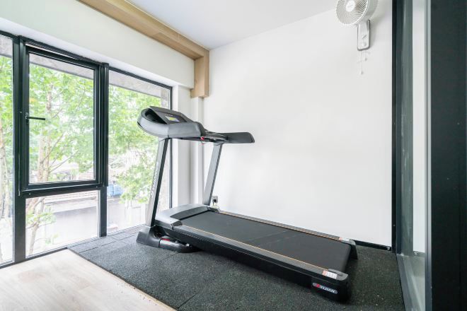 Una cinta de correr en una habitación con un ventanal grande, un ventilador y una puerta que da al exterior.
