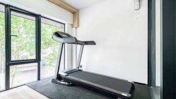 Una cinta de correr en una habitación con un ventanal grande, un ventilador y una puerta que da al exterior.