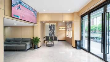 Um saguão de hotel com área de estar, televisão e uma grande janela.