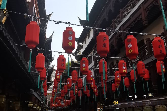A street with traditional architecture and red lanterns hanging overhead.