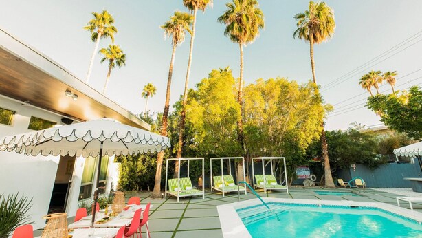 A pool area with lounge chairs, a covered seating area, and tall palm trees. - 5 Private Rooms Sleeps 14 Wesley Studio Buyout (Palm Springs)