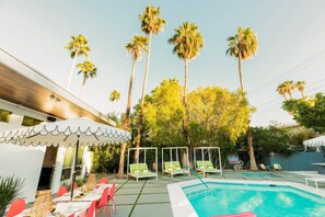Un espace piscine avec des chaises longues, un coin salon abrité et de grands palmiers.
