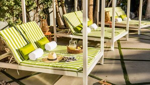 Outdoor lounge chairs with striped cushions, a wicker basket with a drink, and a straw hat on the ground. - 5 Private Rooms Sleeps 14 Wesley Studio Buyout (Palm Springs)
