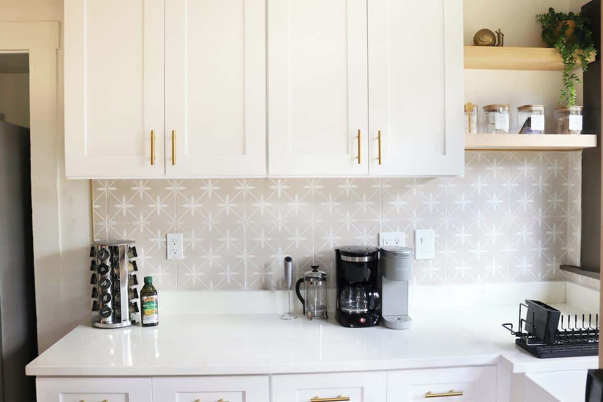 Una cocina con armarios blancos, cafetera, especiero y una planta en un estante.