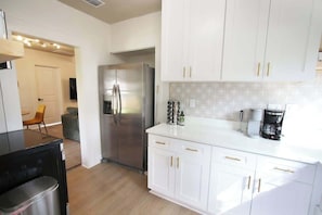 A modern kitchen with white cabinets, a stainless steel refrigerator, and a coffee maker.