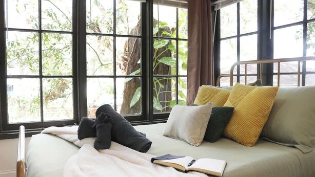 A bed with a white blanket and pillows, a book, and a window with a view of trees. - Walkable Outdoor Oasis BBQ Firepit and Bocce Ball (Tampa)