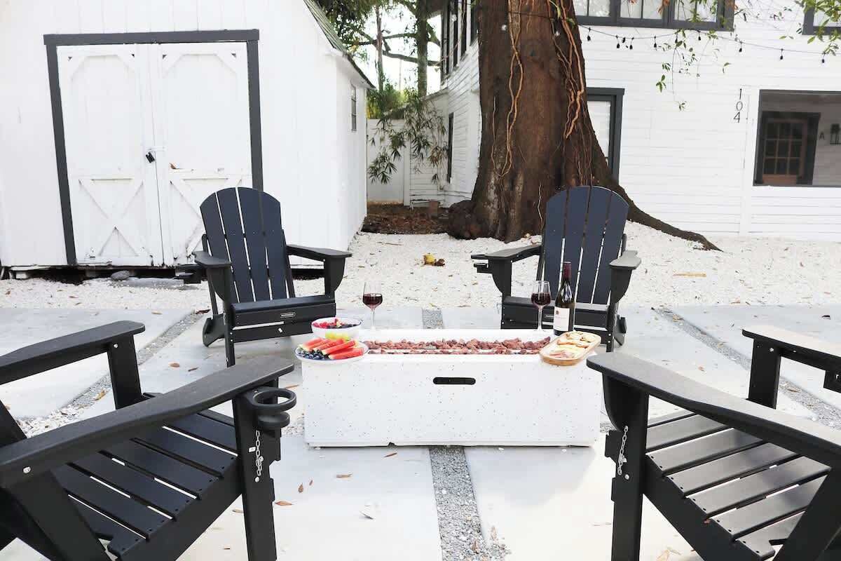 Une terrasse avec des fauteuils Adirondack, un foyer et une table dressée avec de la nourriture et des boissons.