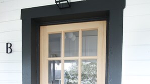 A wooden door with a black frame, a small window, and a black light fixture above it. - Walkable Outdoor Oasis BBQ Firepit and Bocce Ball (Tampa)