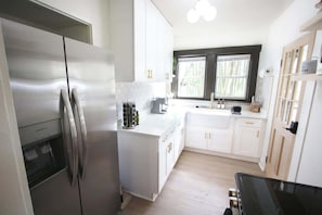 A modern kitchen with white cabinets, a stainless steel refrigerator, and a window with a view of greenery.