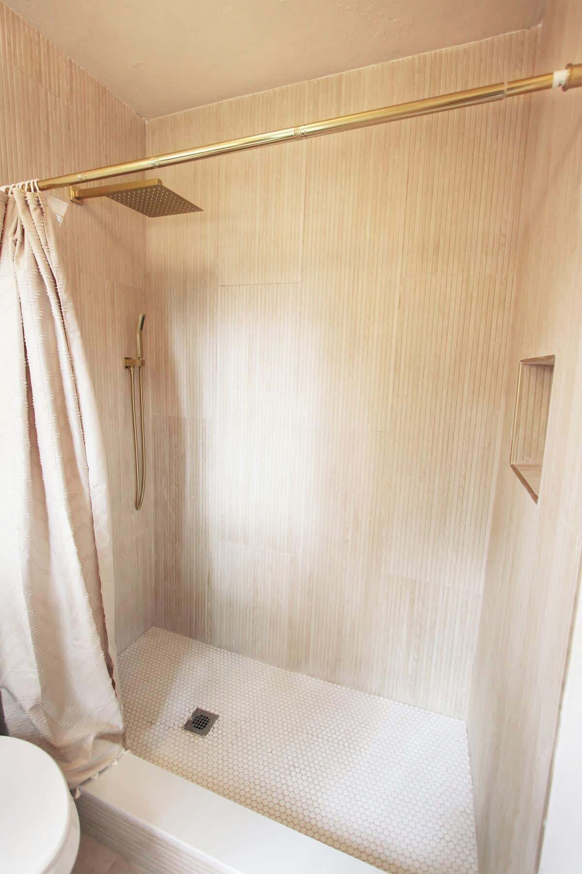 Ducha con cabezal dorado y cortina, una ventana pequeña y piso de baldosas.